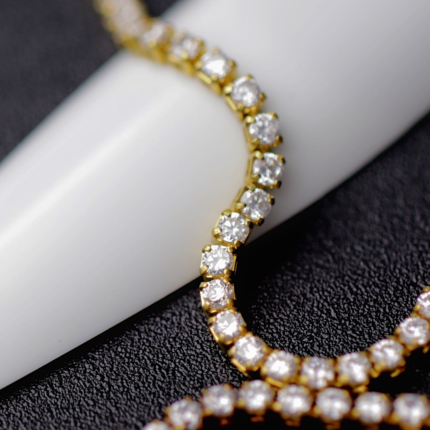 Gold 1.2 mm clear zirconia rhinestone nail art chain wrapped around a white nail tip on a black background