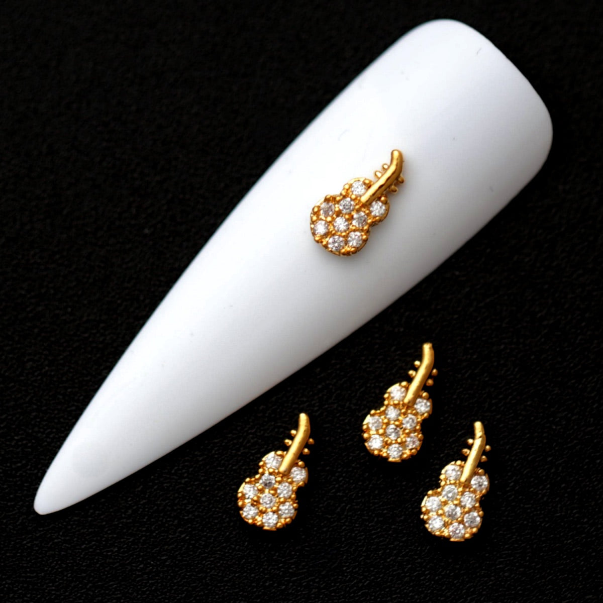 Gold guitar nail charms paved with crystal CZ stones on a white nail tip against a black background