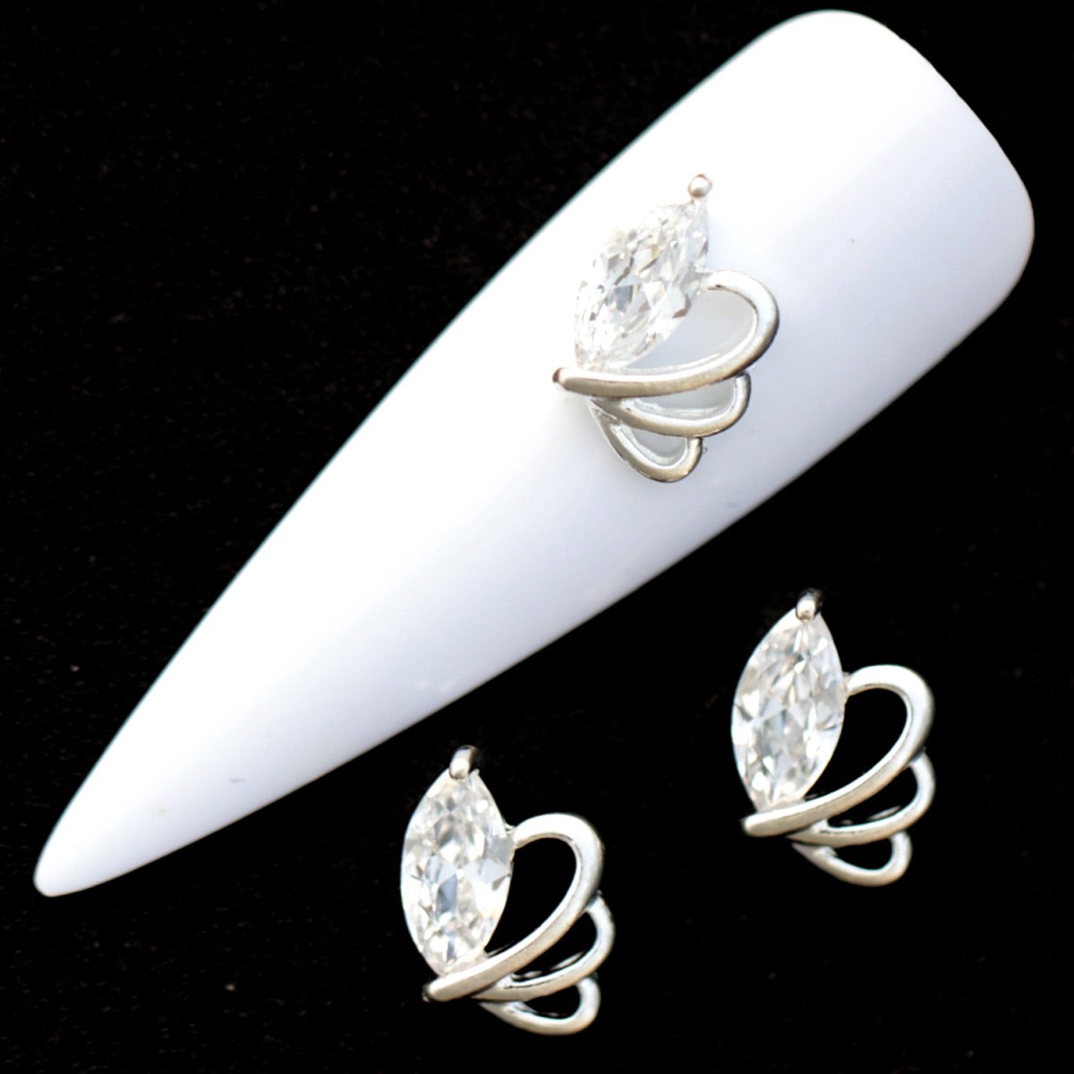 Silver butterfly nail charms with large marquise crystal CZ stones and silver loop wings on a white nail tip against a black background.