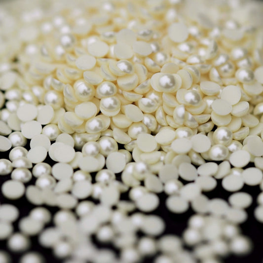 A pile of small 2 mm eggshell acrylic half pearls scattered across a dark surface.