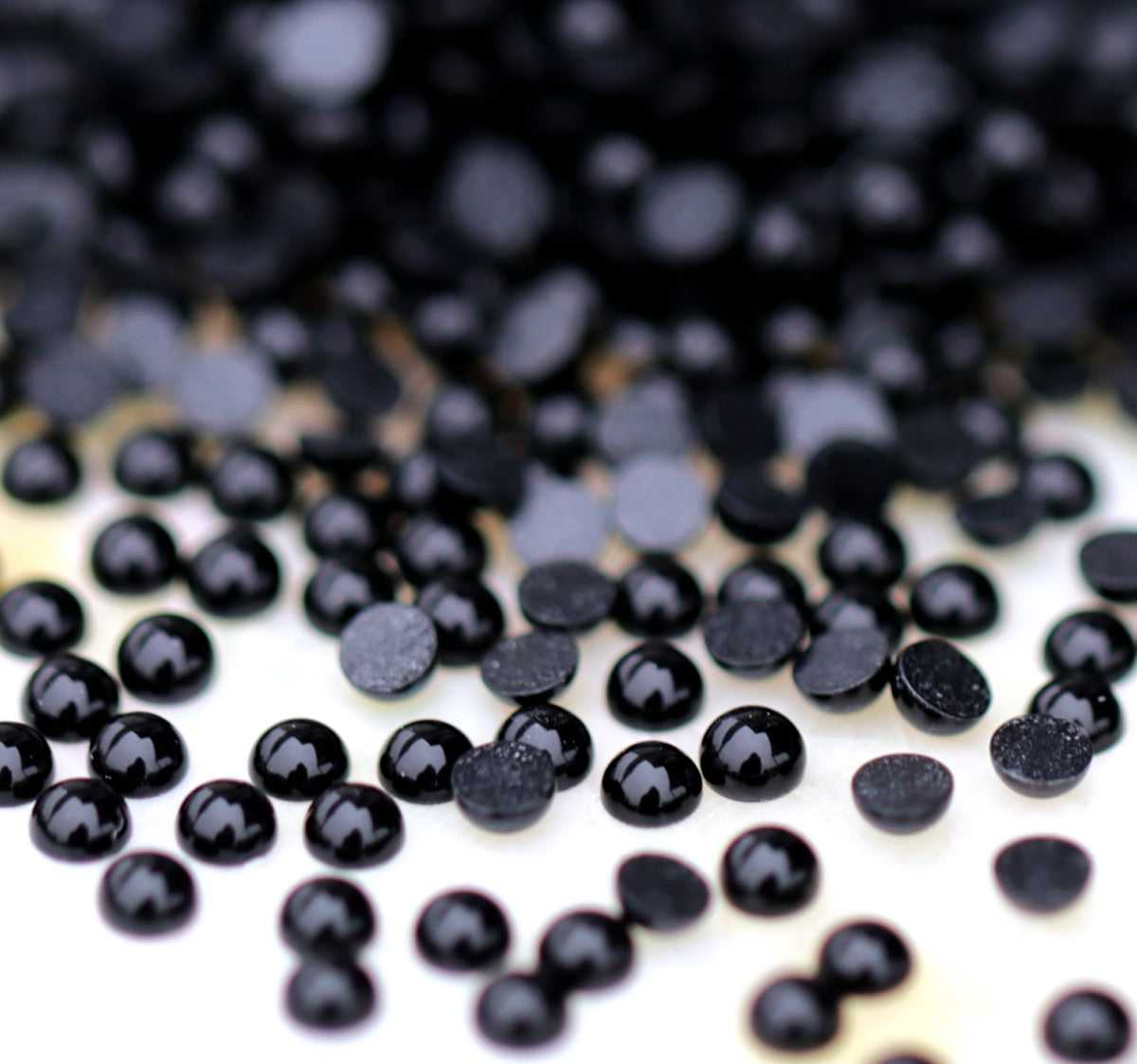 A scatter of tiny Jet black acrylic half pearls with glossy domed tops and flat backs on a light surface.