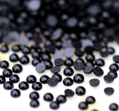A scatter of tiny Jet black acrylic half pearls with glossy domed tops and flat backs on a light surface.