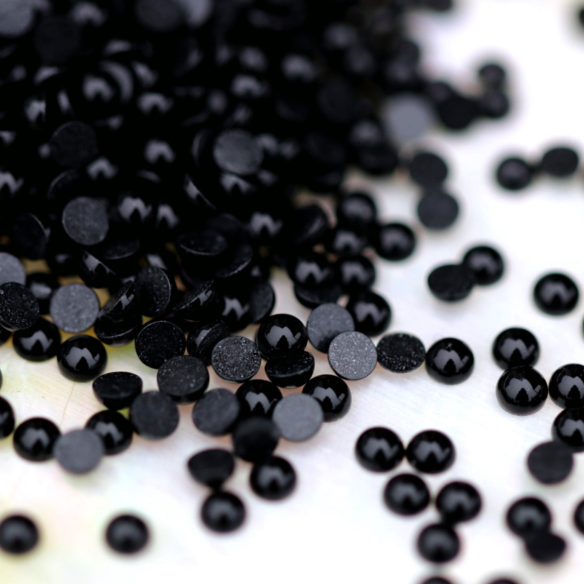 A scatter of tiny Jet black acrylic half pearls with glossy domed tops and flat backs on a light surface.