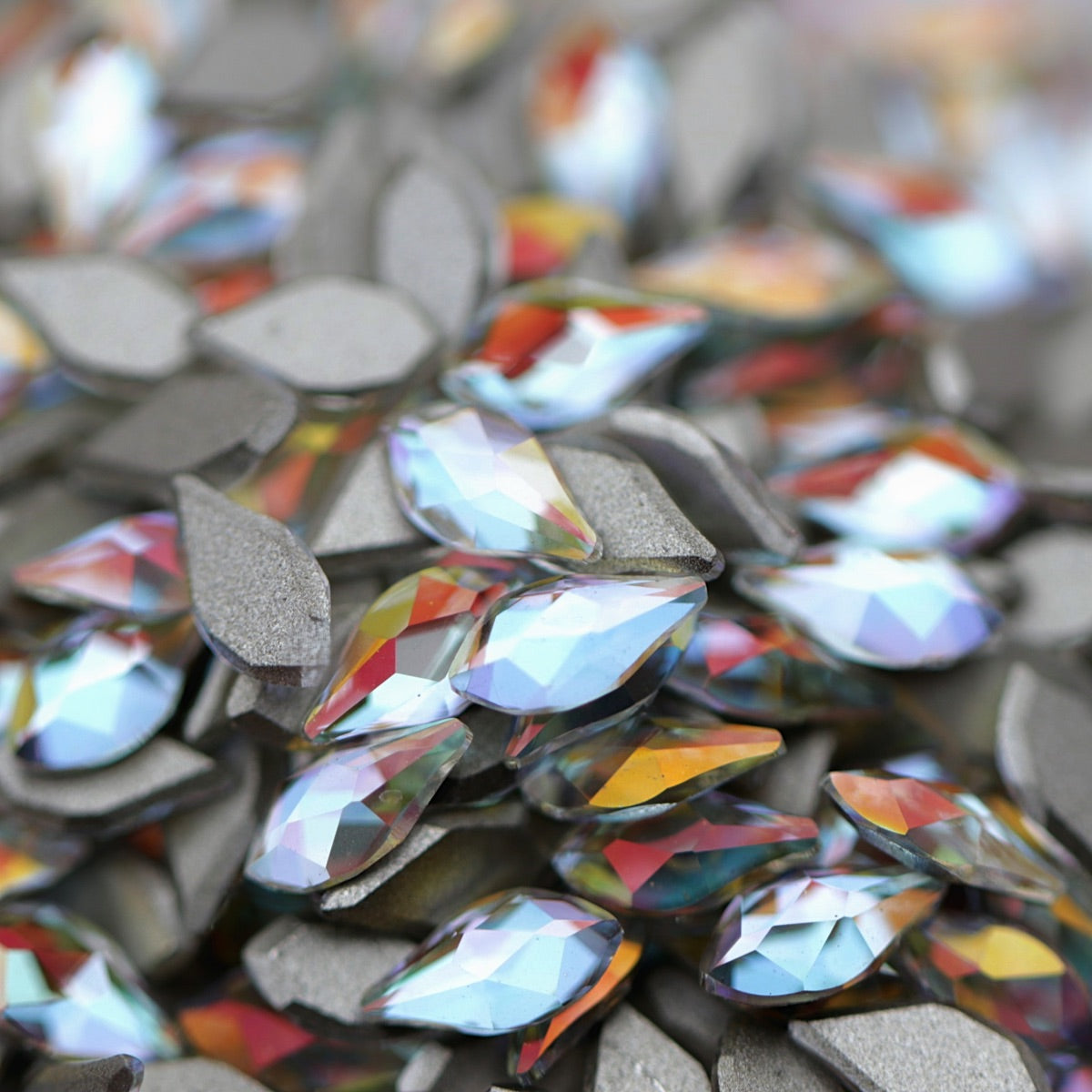 Crystal Gold Shimmer flame-shaped K9 flatback crystals with icy-clear base, soft blue undertone, and golden reflections scattered on a surface.