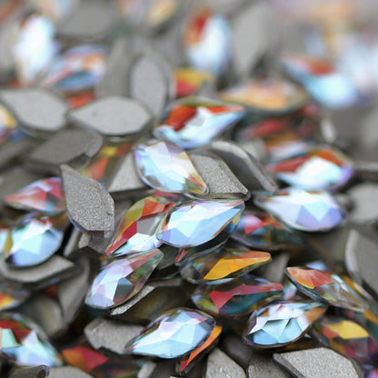 Crystal Gold Shimmer flame-shaped K9 flatback crystals with icy-clear base, soft blue undertone, and golden reflections scattered on a surface.