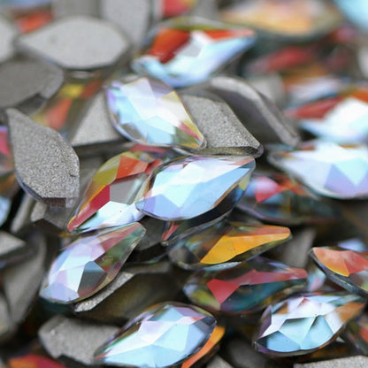 Crystal Gold Shimmer flame-shaped K9 flatback crystals with icy-clear base, soft blue undertone, and golden reflections scattered on a surface.