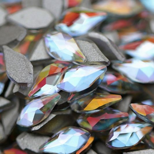 Crystal Gold Shimmer flame-shaped K9 flatback crystals with icy-clear base, soft blue undertone, and golden reflections scattered on a surface.