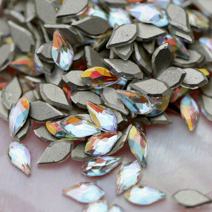 Crystal Gold Shimmer flame-shaped K9 flatback crystals with icy-clear base, soft blue undertone, and golden reflections scattered on a surface.