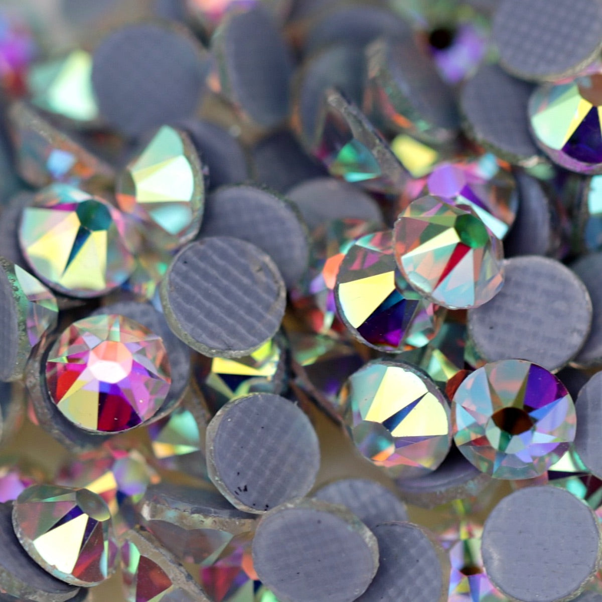 Close-up of round Crystal AB Eunails hotfix rhinestones with faceted tops and grey textured hotfix backs scattered on a light surface.