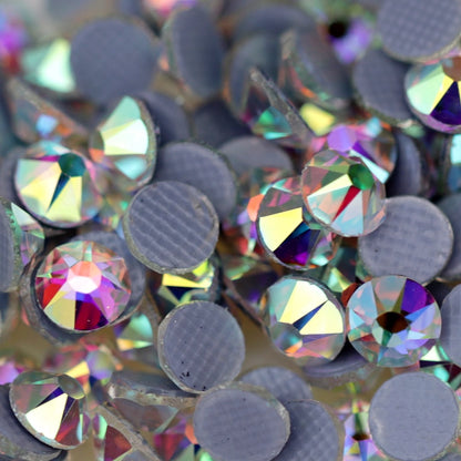 Close-up of round Crystal AB Eunails hotfix rhinestones with faceted tops and grey textured hotfix backs scattered on a light surface.