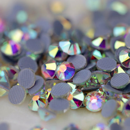 Close-up of round Crystal AB Eunails hotfix rhinestones with faceted tops and grey textured hotfix backs scattered on a light surface.