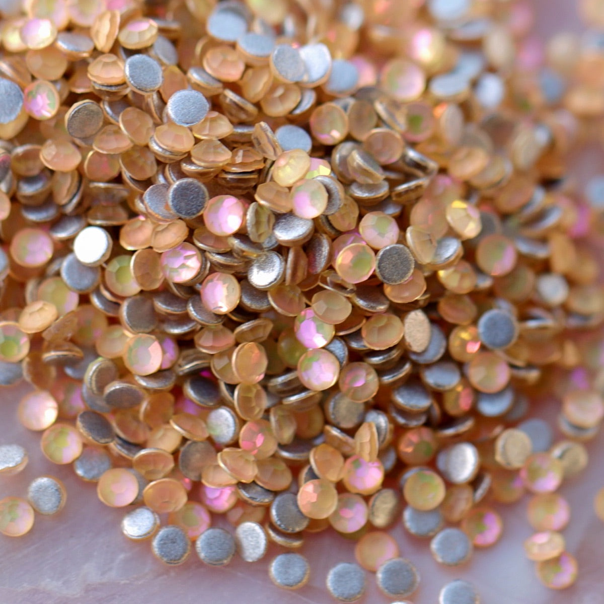 Pile of round flatback rhinestones in Cream Pie color with champagne gold shimmer and pearl iridescence on light background for nail art