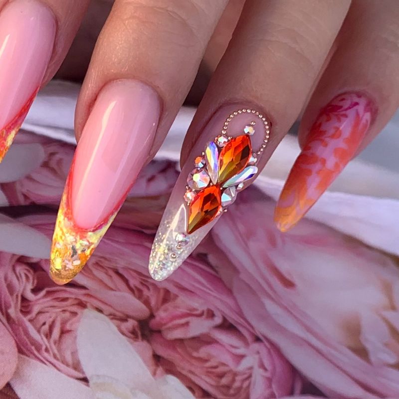 Nail art with multicolored flatback rhinestone shapes arranged on a stiletto nail, illustrating how different crystal brands and shapes can be combined in creative designs