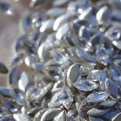 Clear flatback zircon marquise crystals scattered on an iridescent background, showing pointed oval stones ideal for detailed nail art and embellishments