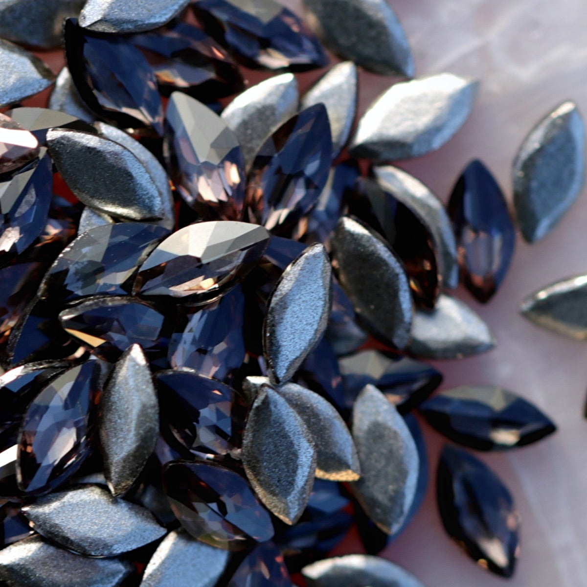 Pile of Damson marquise flatback zircons showing silvery-purple tones on light background for nail art