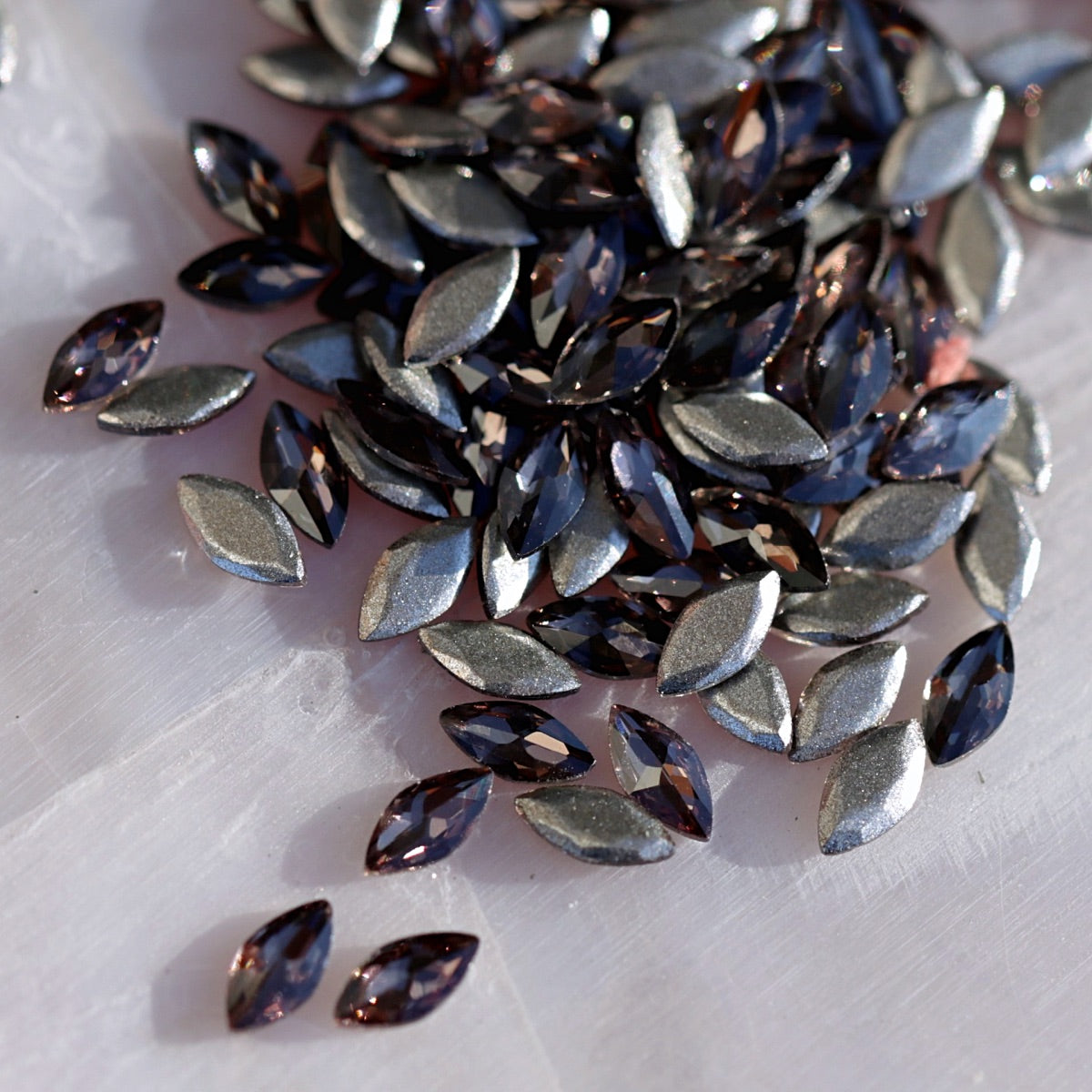 Scattered Damson color marquise crystals with grayish-lilac metallic facets and high reflectivity for nail decoration