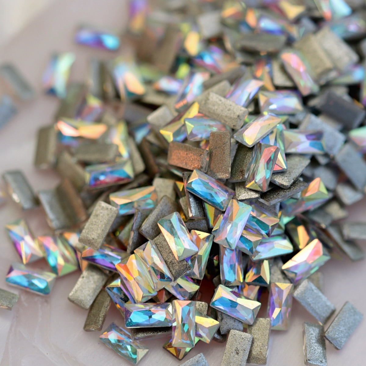 Iridescent Crystal AB flatback zircon baguette crystals in 3x1.5mm size scattered on a light background, showing elongated rectangular stones for nail art and decorations.