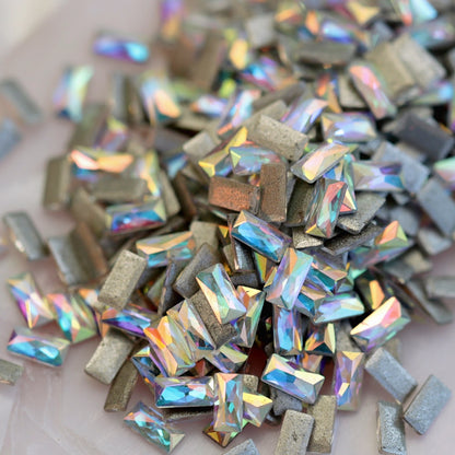 Iridescent Crystal AB flatback zircon baguette crystals in 3x1.5mm size scattered on a light background, showing elongated rectangular stones for nail art and decorations.