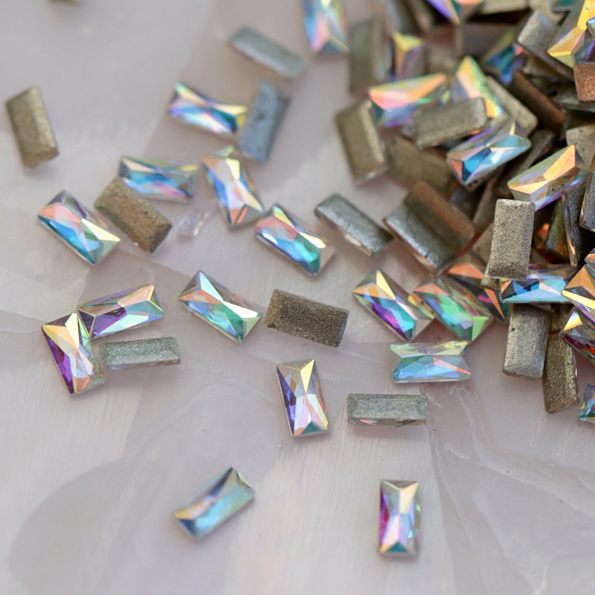 Iridescent Crystal AB flatback zircon baguette crystals in 3x1.5mm size scattered on a light background, showing elongated rectangular stones for nail art and decorations.