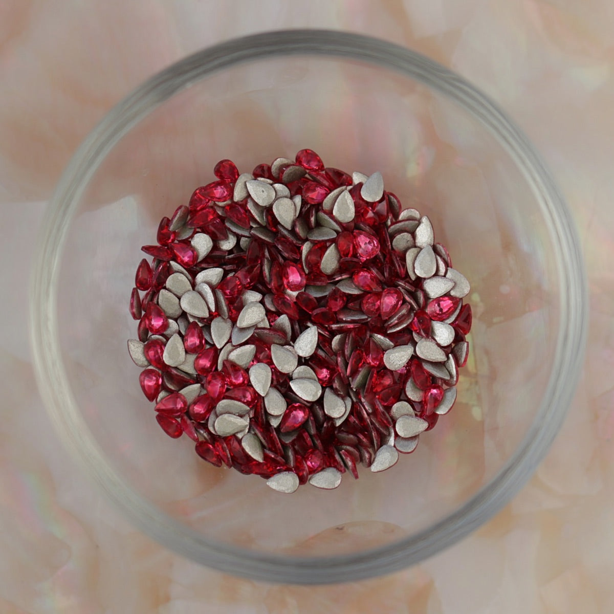 Glass bowl filled with Flatback Zircon Nail Art Drop Deep Pink crystals, showing many bright pink teardrop stones with silver flatbacks ready for nail art and decorations.