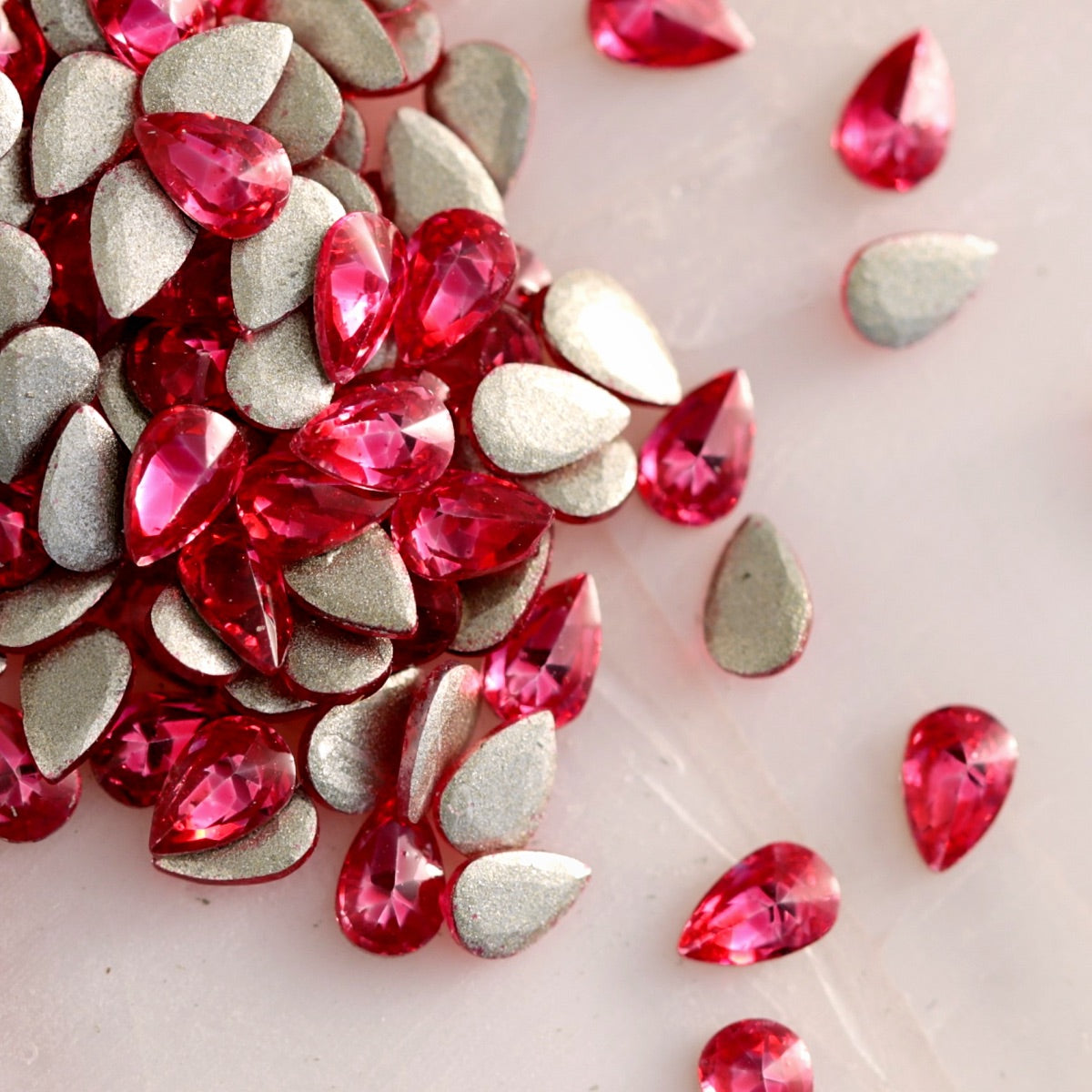 Flatback Zircon Nail Art Drop Deep Pink stones scattered on a light surface, displaying vivid pink teardrop crystals alongside their metallic foil backs.