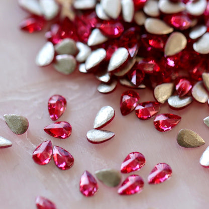 Flatback Zircon Nail Art Drop Deep Pink stones scattered on a light surface, displaying vivid pink teardrop crystals alongside their metallic foil backs.