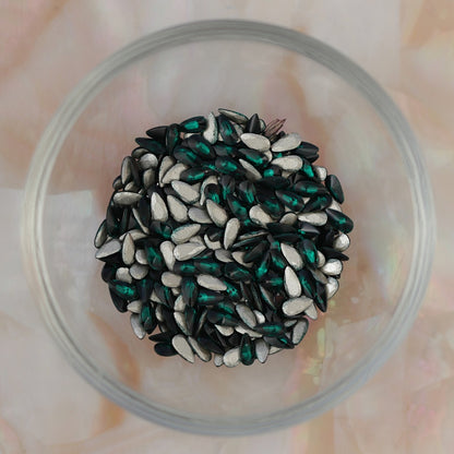 Glass bowl filled with Flatback Zircon Nail Art Drop Emerald crystals, showing many deep green teardrop stones with silver flatbacks ready for nail art and decorations.