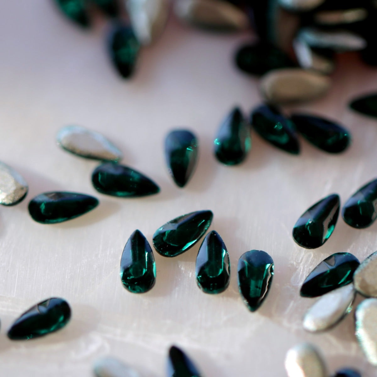 Close-up of Flatback Zircon Nail Art Drop Emerald crystals, highlighting the deep emerald color and faceted teardrop shape perfect for detailed nail designs.