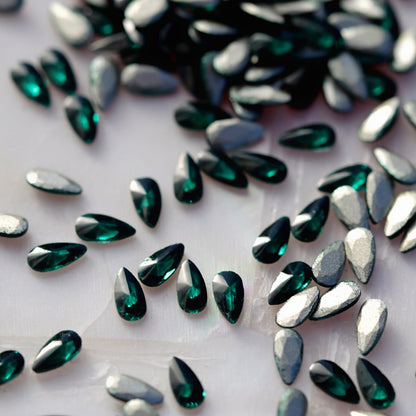 Flatback Zircon Nail Art Drop Emerald stones scattered on a light surface, displaying the rich green teardrop crystals alongside their metallic foil backs.