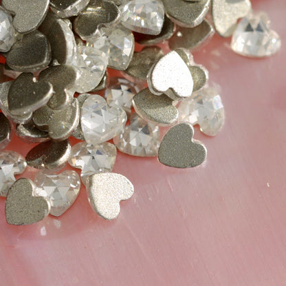 Pile of 3x3mm clear flatback zircon heart rhinestones with silver foil backing on pearlescent pink background for romantic nail art