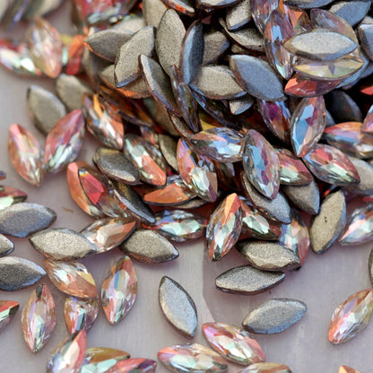 Close-up of Flatback Zircon Marquise Copper AB rhinestones, highlighting the faceted navette shape and glowing peach-gold iridescent finish used for creative nail designs.