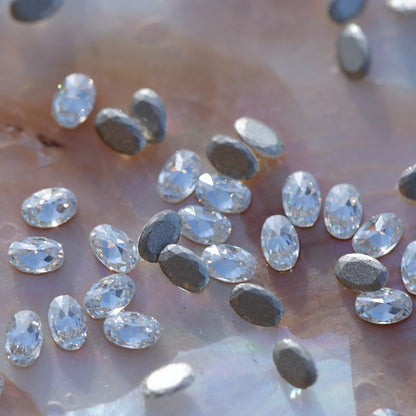 Close-up of sparkling clear oval-shaped flatback zircon crystals with metallic silver backs, perfect for classic and elongated nail embellishments