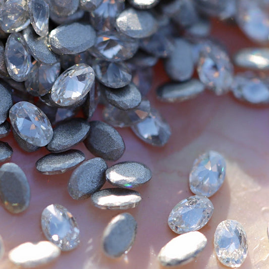 Clear flatback zircon oval crystals scattered on an iridescent background, showing smooth oval stones ideal for elegant nail art designs