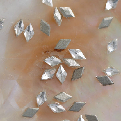 Closeup of flatback zircon rhombus shaped crystals showing silver glitter and clear faceted surfaces on soft pearl backdrop for nail design application