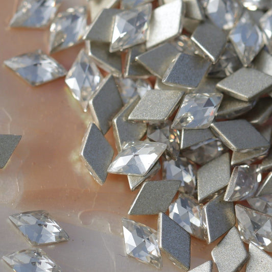 Pile of metallic silver rhombus flatback zircon crystals on pearlescent background for nail art embellishments