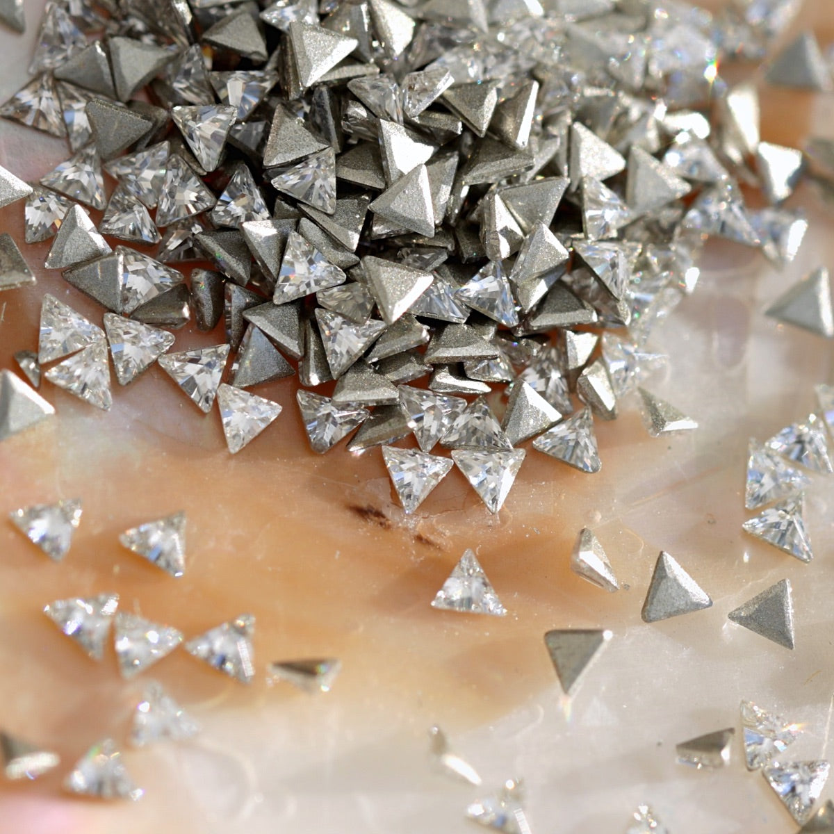 Closeup view of flatback zircon triangle shaped crystals displaying silver metallic and clear faceted finishes on pearlescent surface for nail decoration