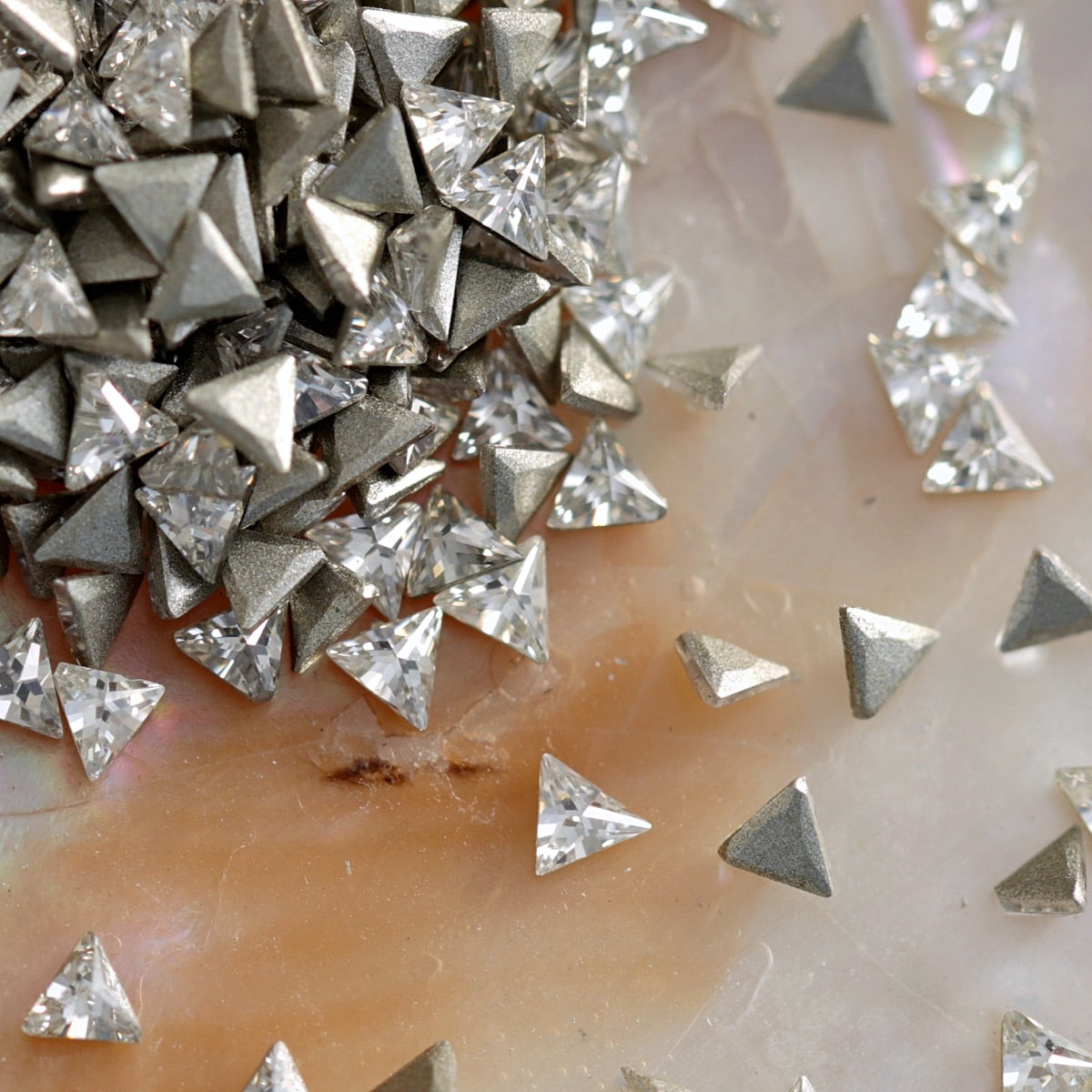 Flatback zircon triangle crystals in metallic silver tones arranged on pearl background, ideal for 3D nail art embellishments