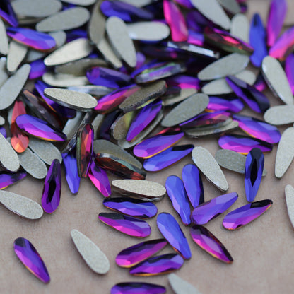 Slim flatback raindrop glass rhinestones in Meridian Blue showing blue, violet and pink reflections scattered on a surface.