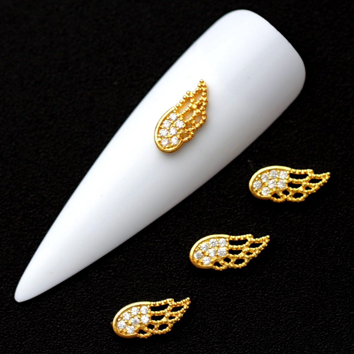 Gold angel wing nail charms paved with crystal CZ stones on a white nail tip against a black background