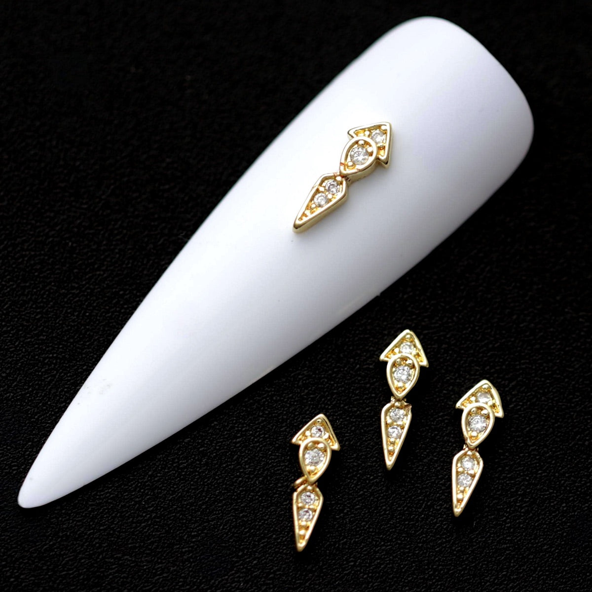Gold arrow marquise nail charms paved with crystal cubic zirconia on a white nail tip against a black background
