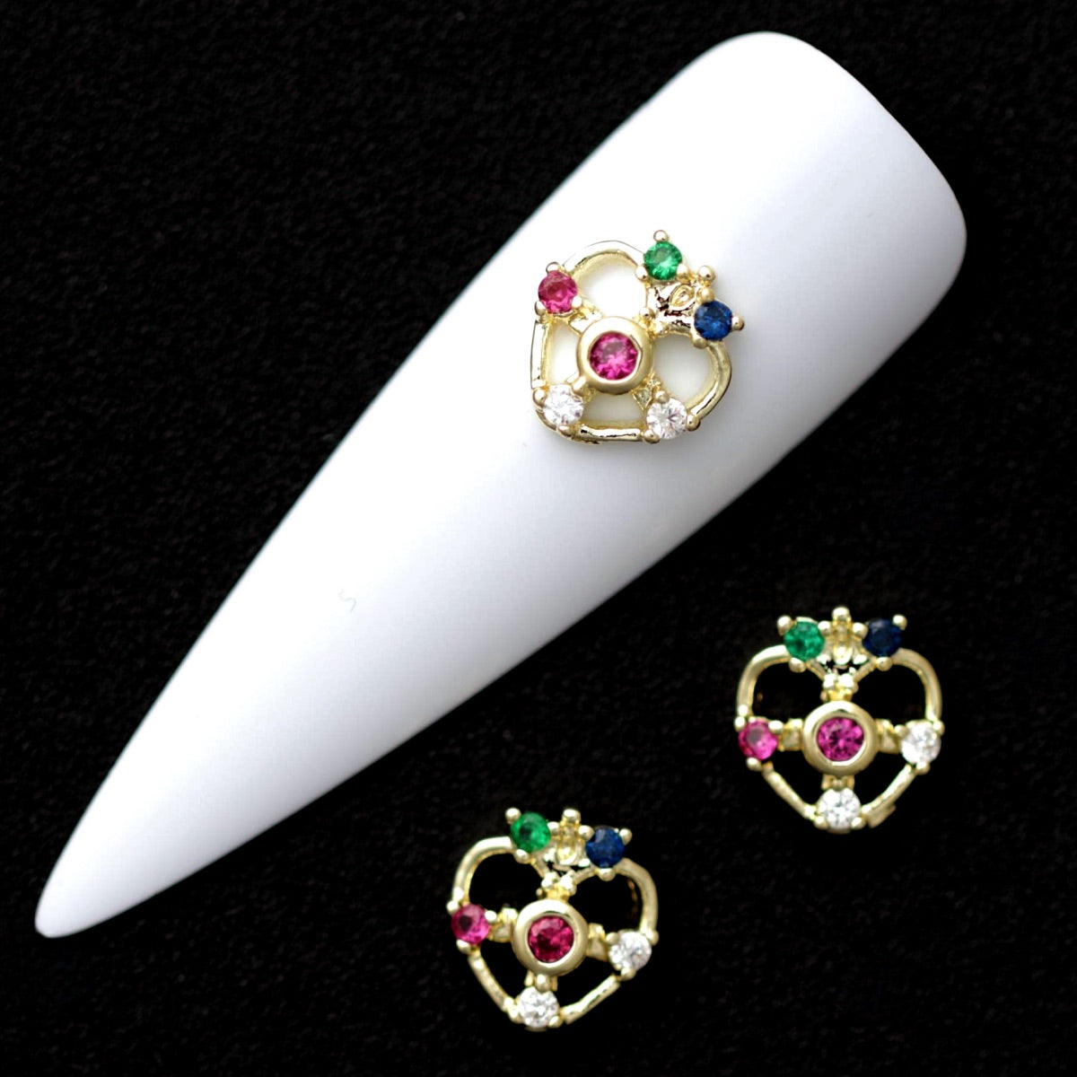 8 mm crown-topped heart nail charms with pink, green, blue and crystal CZ stones displayed on a white nail tip against a black background