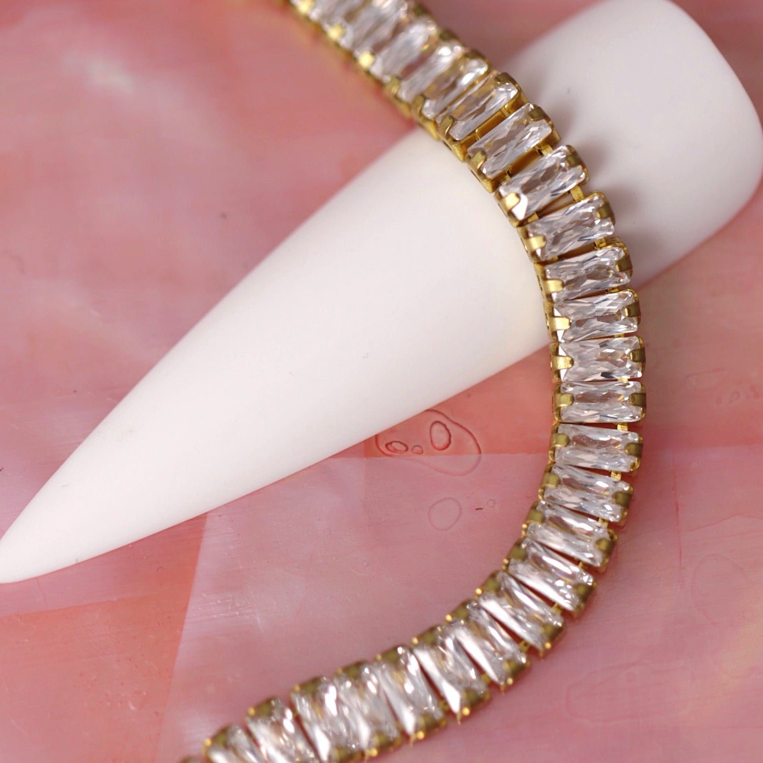 Gold 4×2 mm clear zirconia baguette rhinestone nail art chain wrapped around a white nail tip on a pink background