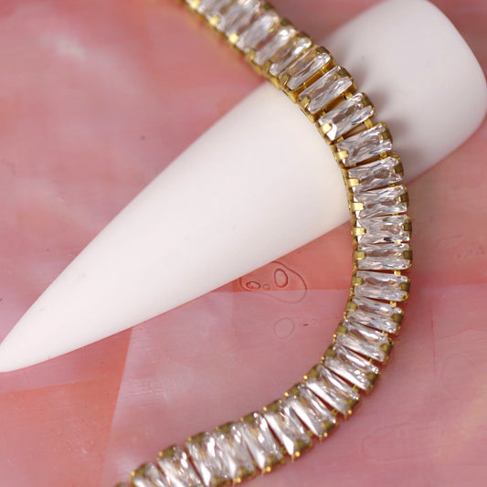 Gold 4×2 mm clear zirconia baguette rhinestone nail art chain wrapped around a white nail tip on a pink background