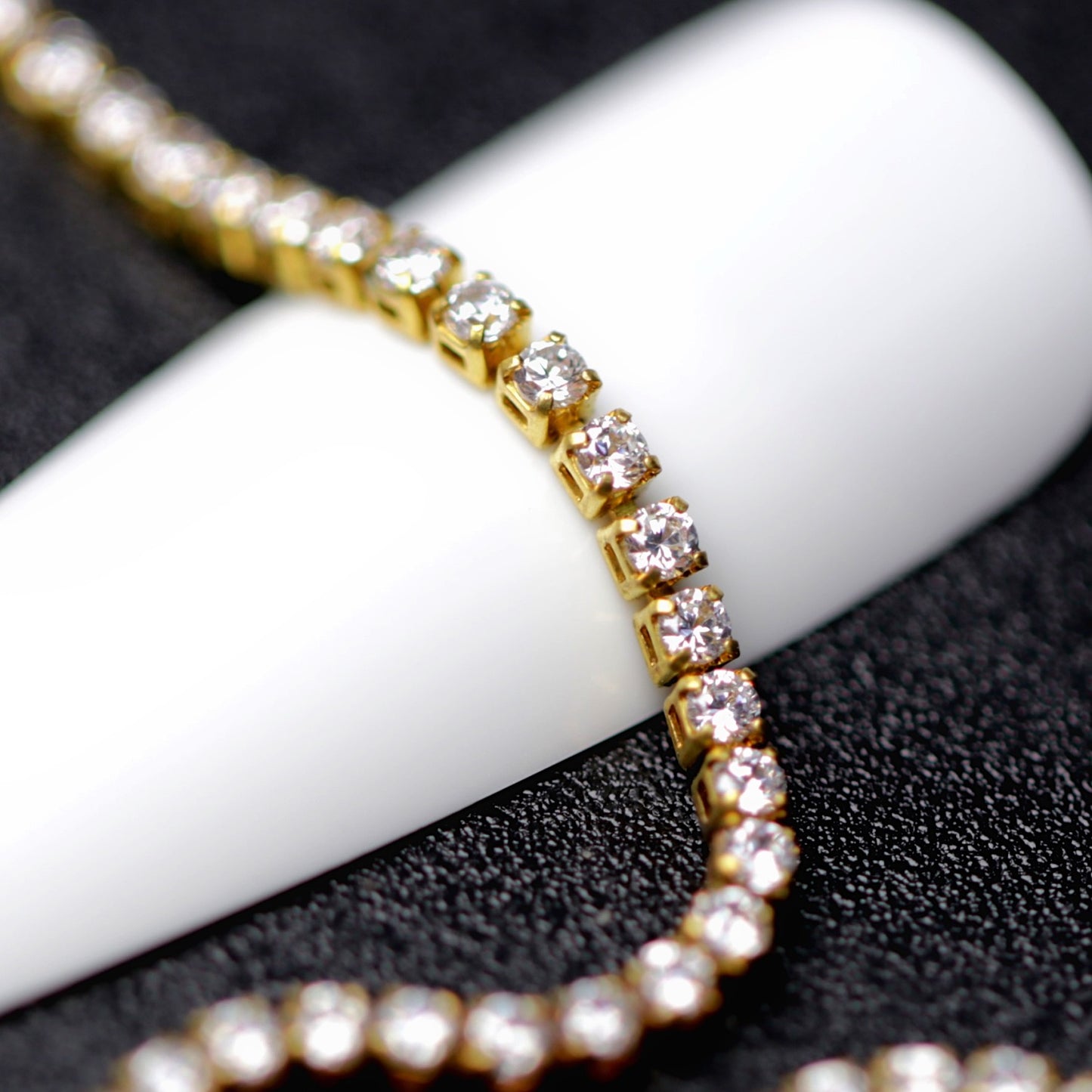 Gold 1.2 mm clear zirconia rhinestone nail art chain wrapped around a white nail tip on a black background