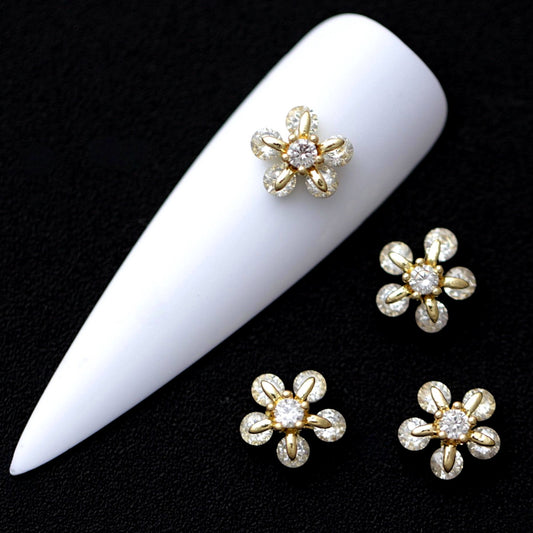 Gold daisy flower nail charms with central crystal CZ and crystal bead petals on a white nail tip against a black background