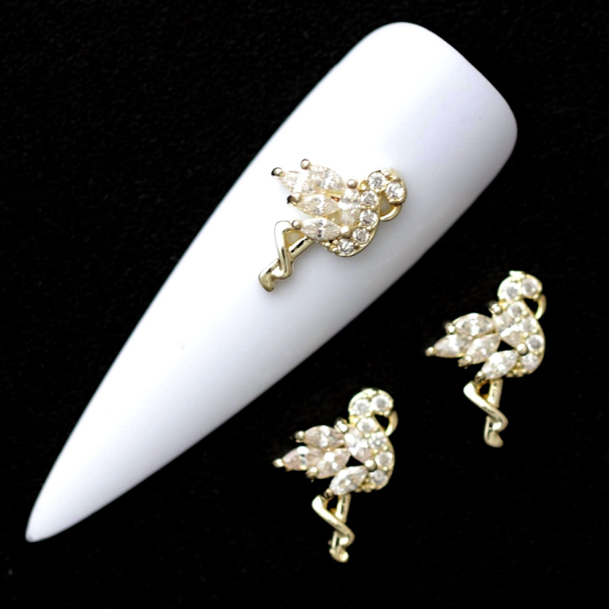 Gold 12×8 mm flamingo nail charms paved with crystal CZ stones displayed on a white nail tip against a black background