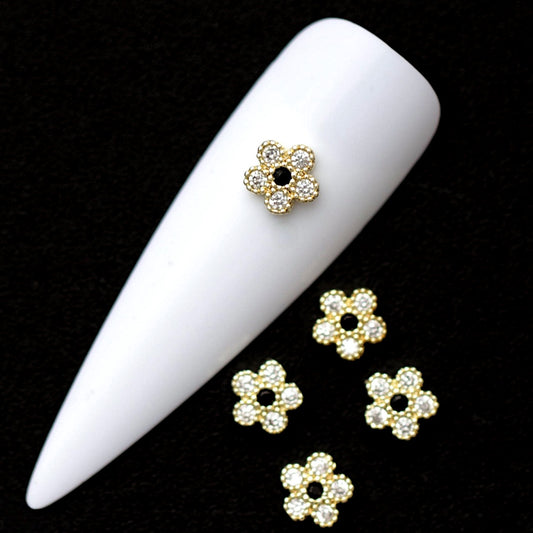 Gold 5 mm flower-shaped nail charms with crystal CZ petals and black jet CZ centre displayed on a white nail tip against a black background