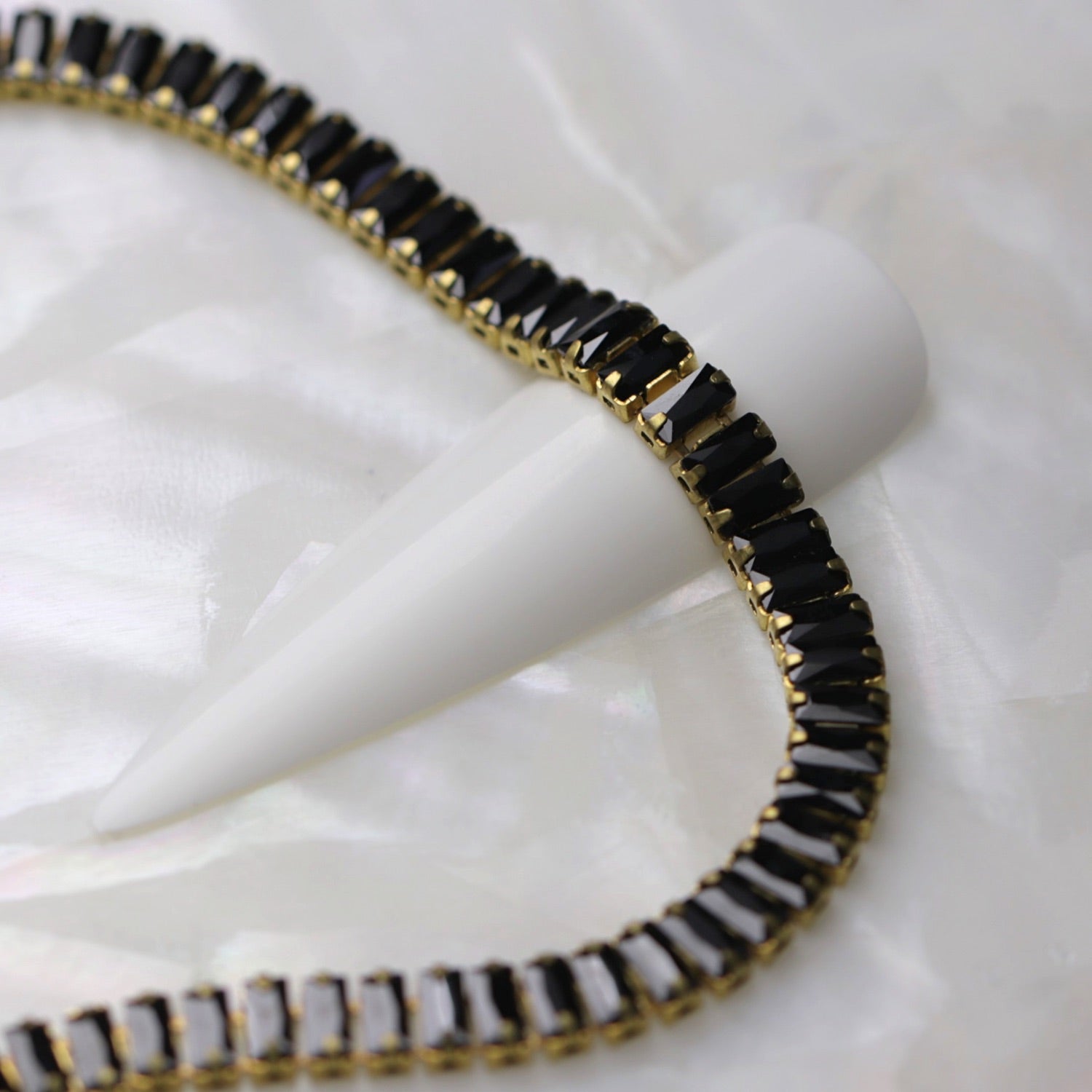 Close-up of gold cup chain with 4×2 mm jet zirconia baguette rhinestones displayed around a white nail tip