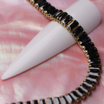 Gold 4×2 mm jet zirconia baguette rhinestone nail art chain wrapped around a white nail tip on a pink background