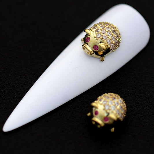 Gold lucky pig nail charms with crystal CZ backs and pink CZ eyes shown on a white nail tip against a black background.